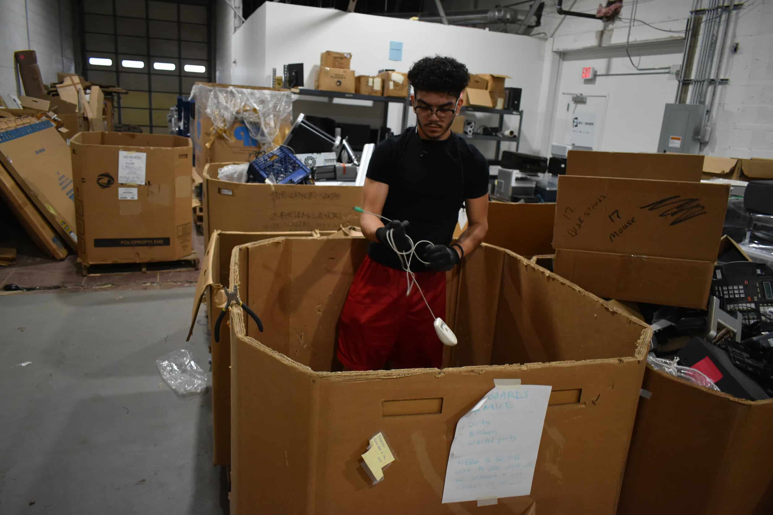 Jovanti Ramirez, a student at CMSD who has a summer internship with PCs for People, works to sort mice and other devices out of a bin in PCs for People’s warehouse in Cleveland. Photo by Conor Morris.