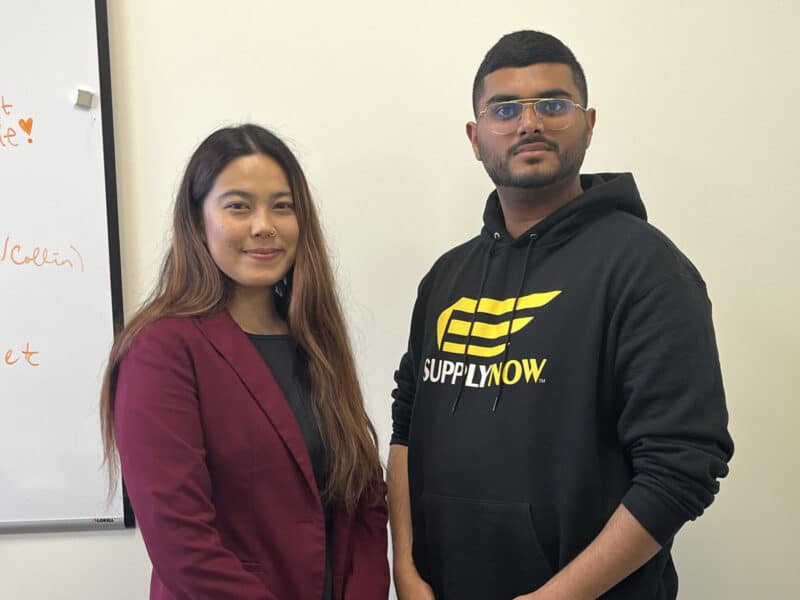 Program training and development manager Supriya Tamang standing next to entrepreneur in residence Aaron George, who is wearing a sweatshirt printed with the name of his company, SupplyNow, inside a meeting room at Global Cleveland’s office.