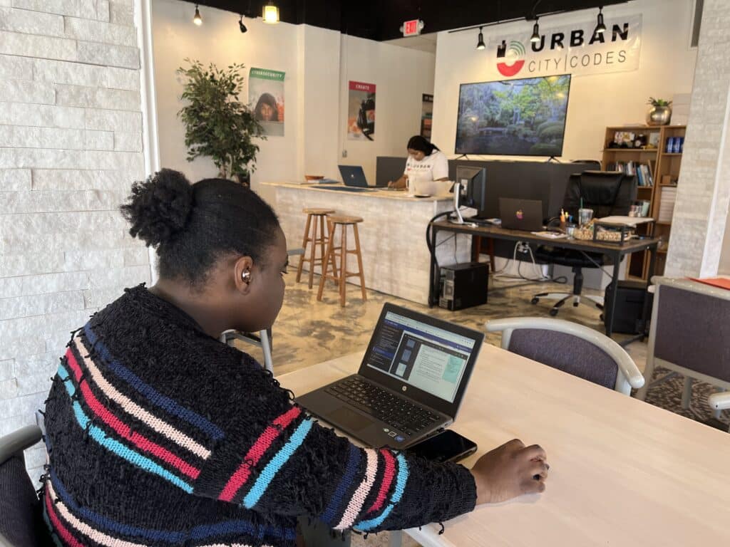 Dayuanna White working on a computer, diagonal to a banner that reads “Urban City Codes” hanging above the front desk. 