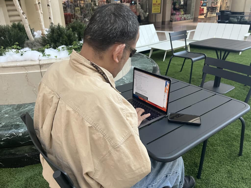 Over-the-shoulder view of Larry Rodriguez navigating the paratransit ride scheduling site as he sits at a table in the park area of Tower City Center. 