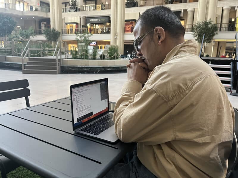 Larry Rodriguez sits in front of his computer at a table in the park area at Tower City Center, resting his head on his folded hands.