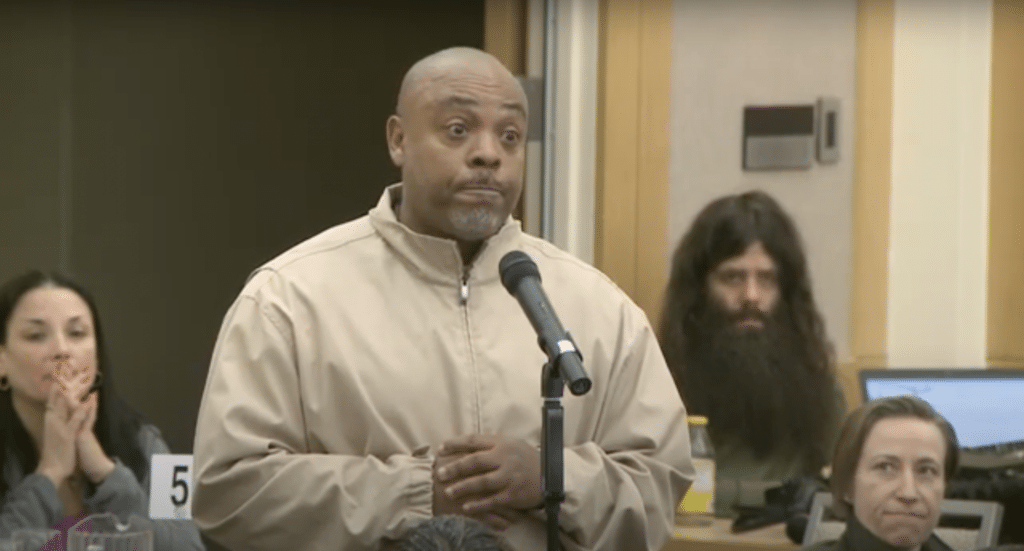 Darrell Houston standing in front of a microphone during the City Club forum as members of the crowd look at him as he shares his story.