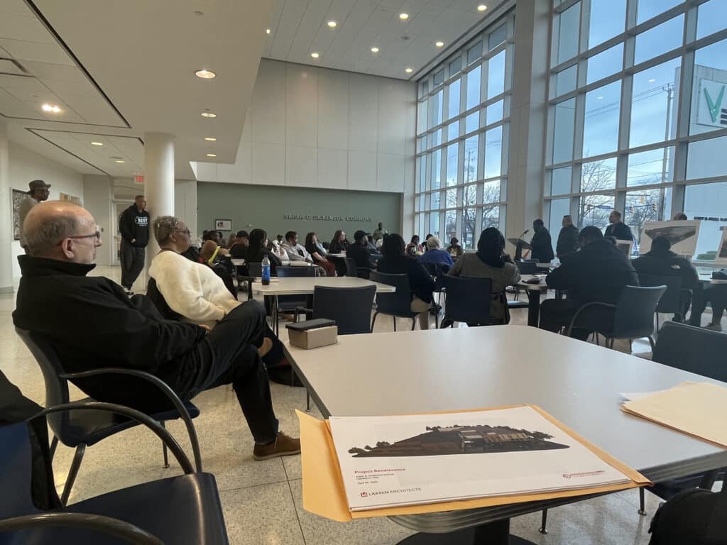 A folder of papers showing renderings of the project plans on a table at the community meeting. 