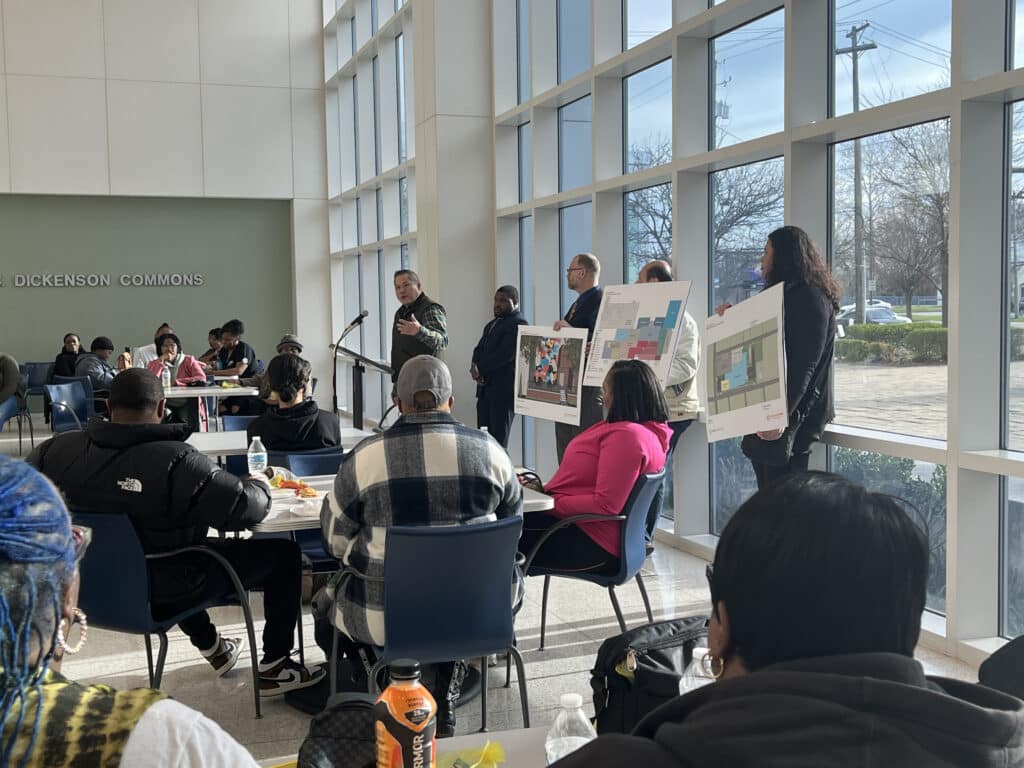 International Food Solutions co-president and co-founder Lincoln Yee at the podium speaking and standing next to Council Member Starr and other project leaders, who are holding signs showing project plans. 