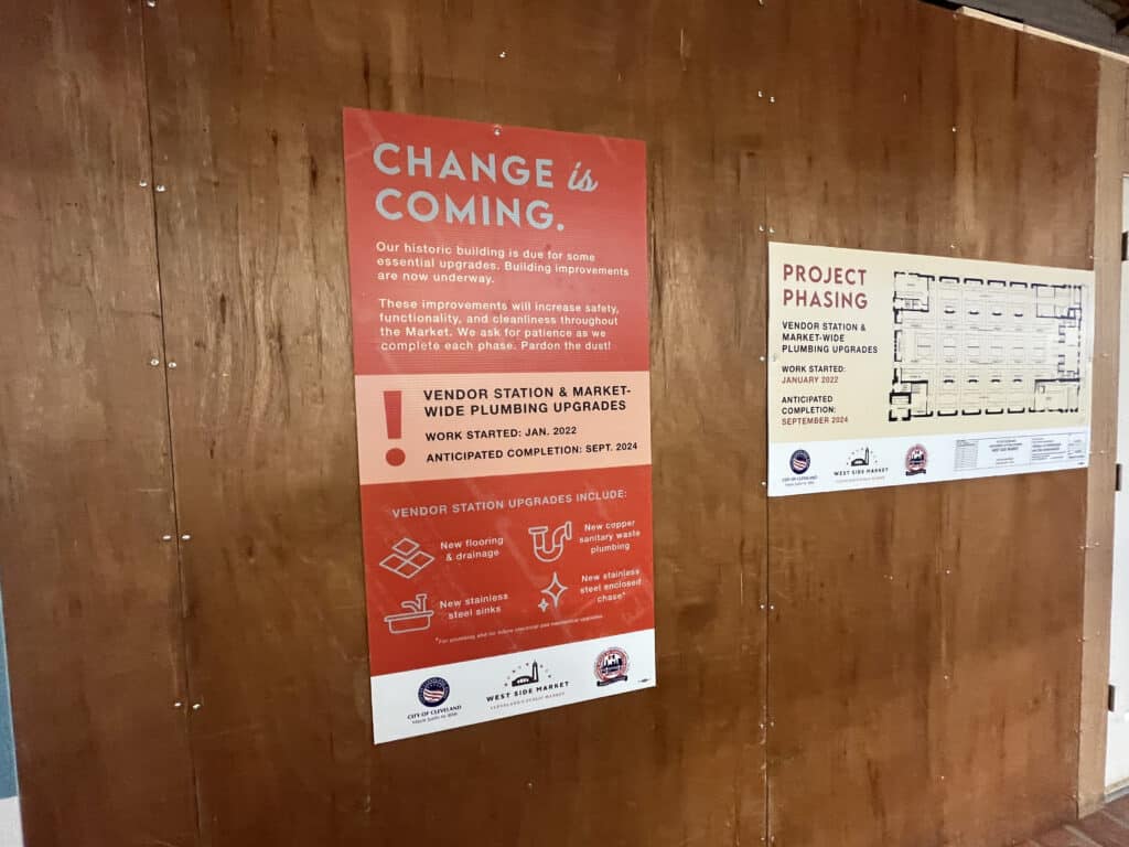Signs inside the Market Hall about the upgrades coming to the market. One of the signs reads, “Change is coming. Our historic building is due for some essential upgrades. Building improvements are now underway. These improvements will increase safety, functionality, and cleanliness throughout the Market. We ask for patience as we complete each phase. Pardon the dust! Vendor station & marketwide plumbing upgrades. Work started: Jan. 2022; Anticipated completion: Sept. 2024. Vendor station upgrades include: new flooring & drainage, new copper sanitary waste plumbing, new stainless steel sinks, and new stainless steel enclosed chase." The second sign reads, “Project phasing” and shows a map of the booths at the market. 