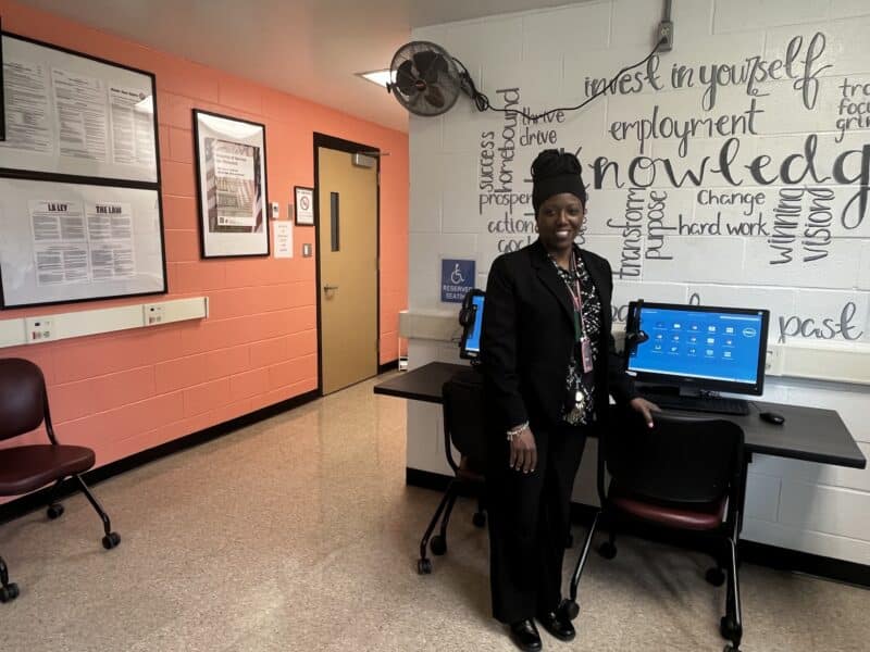 Ohio Means Jobs coordinator Dawn Ballard-Little at the new jobs center, standing in front of a wall, which has words and phrases like “Knowledge,” “education,” “employment,” and “invest in yourself” painted on it.