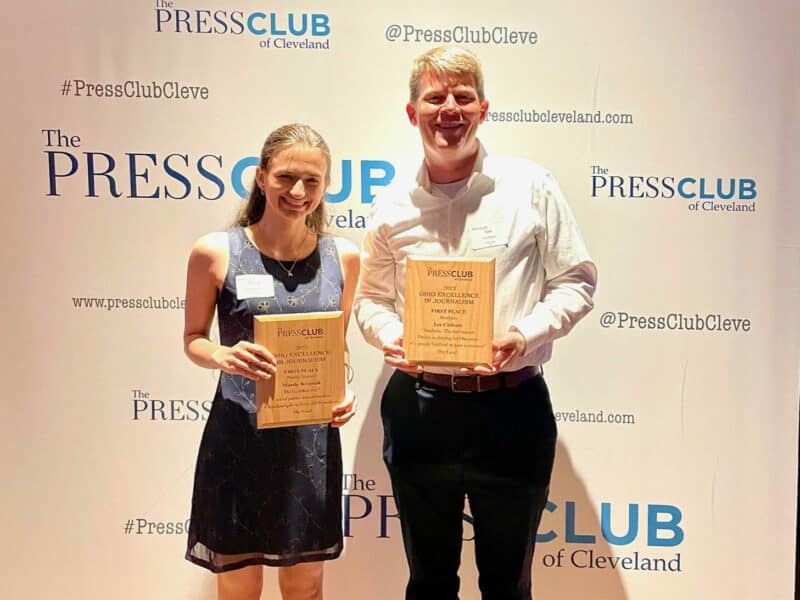 Mandy Kraynak and Lee Chilcote holding their awards and smiling for a photo in front of a Press Club of Cleveland backdrop at the All Ohio Excellence in Journalism awards on Friday, June 2.