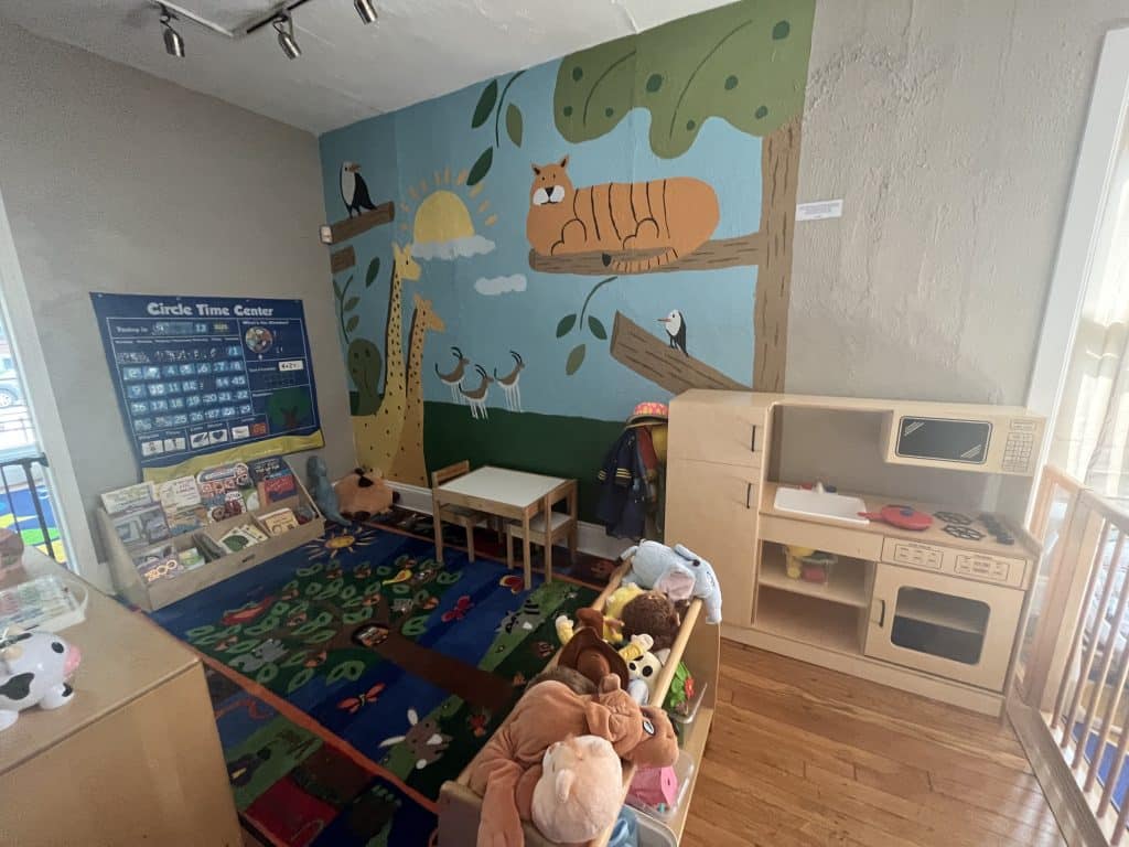 A play area with a jungle animal mural, play kitchen, and shelves of books and stuffed animals.
