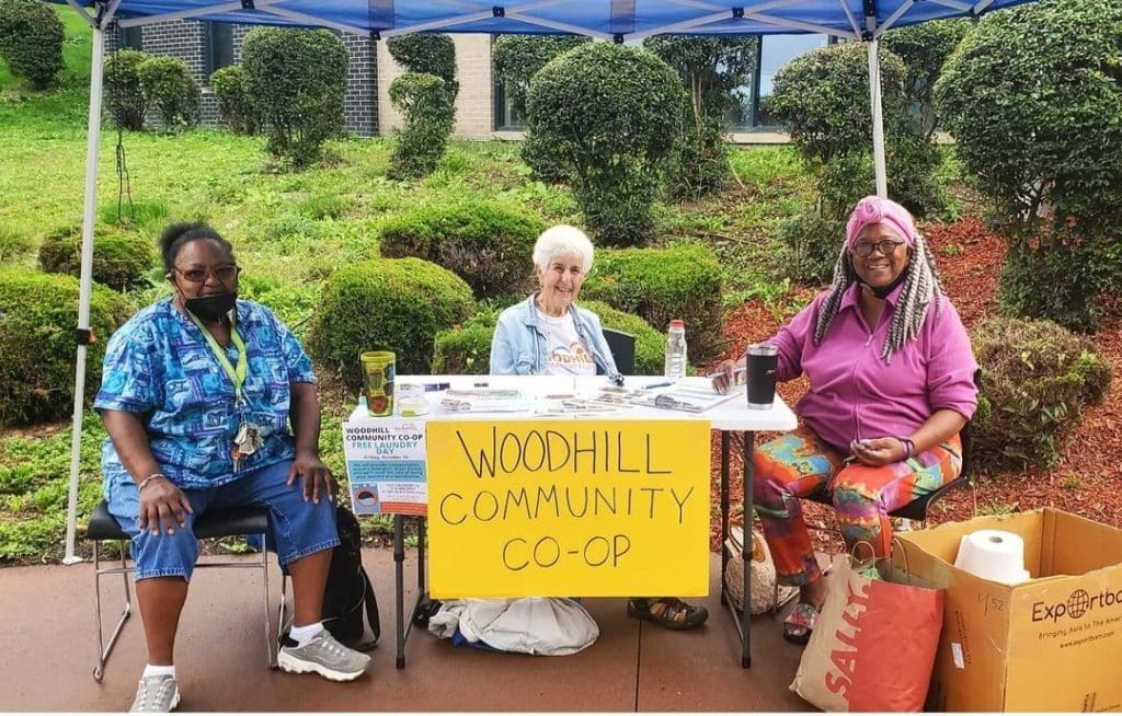 Three people at a table with a Woodhill Community Co-op sign at a laundry day event. 