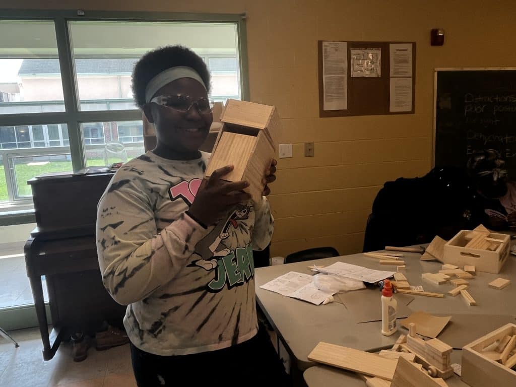 A Rosie’s Girls student smiling and holding one of their projects, a small chest of drawers. 