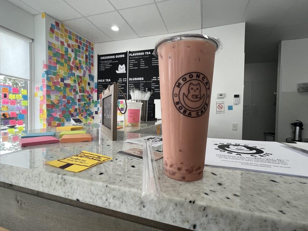 A cup of boba tea on the counter in front of the Post-it note wall and menu.