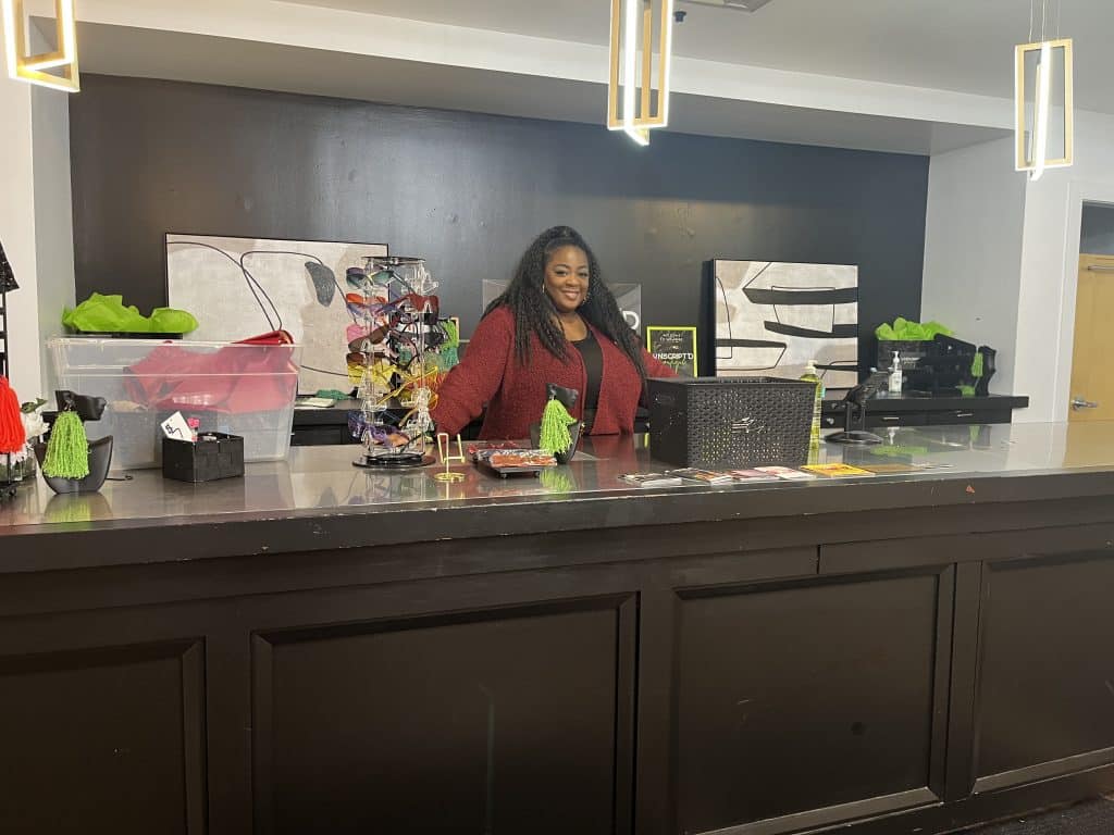 A smiling Black woman stands behind a store counter in Unscript'd Boutique.