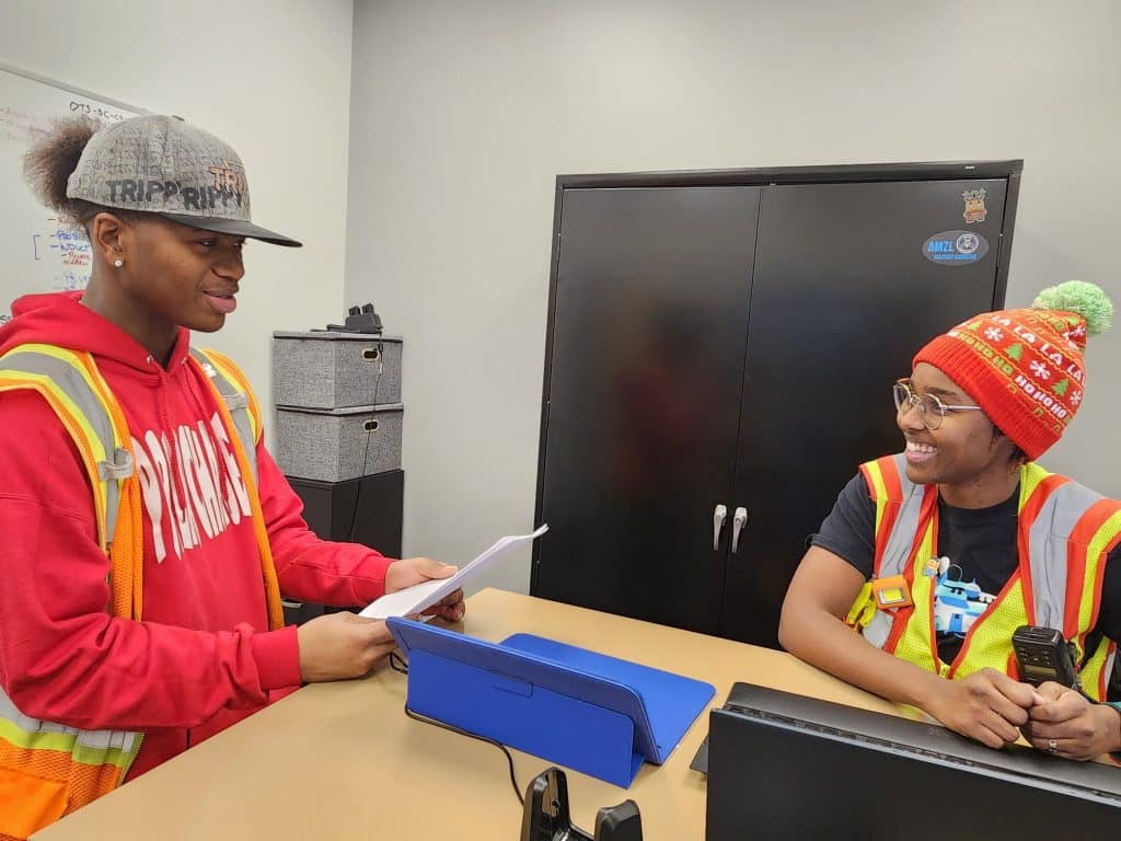 Amazon delivery station associate Oscar Johnson standing around a table with station manager Rebekah Ham at the Amazon DCM3 warehouse. 