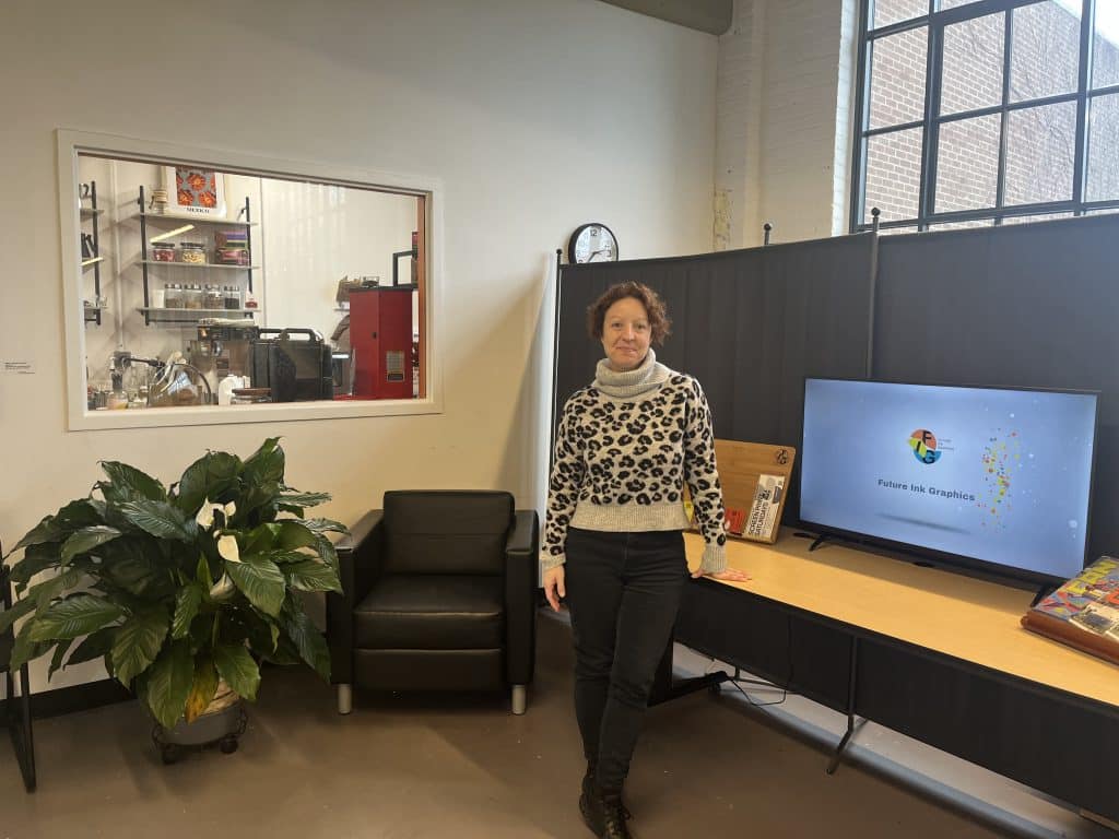 FIG director Stephanie Kluk standing in FIG’s studio space near a window into the coffee shop.