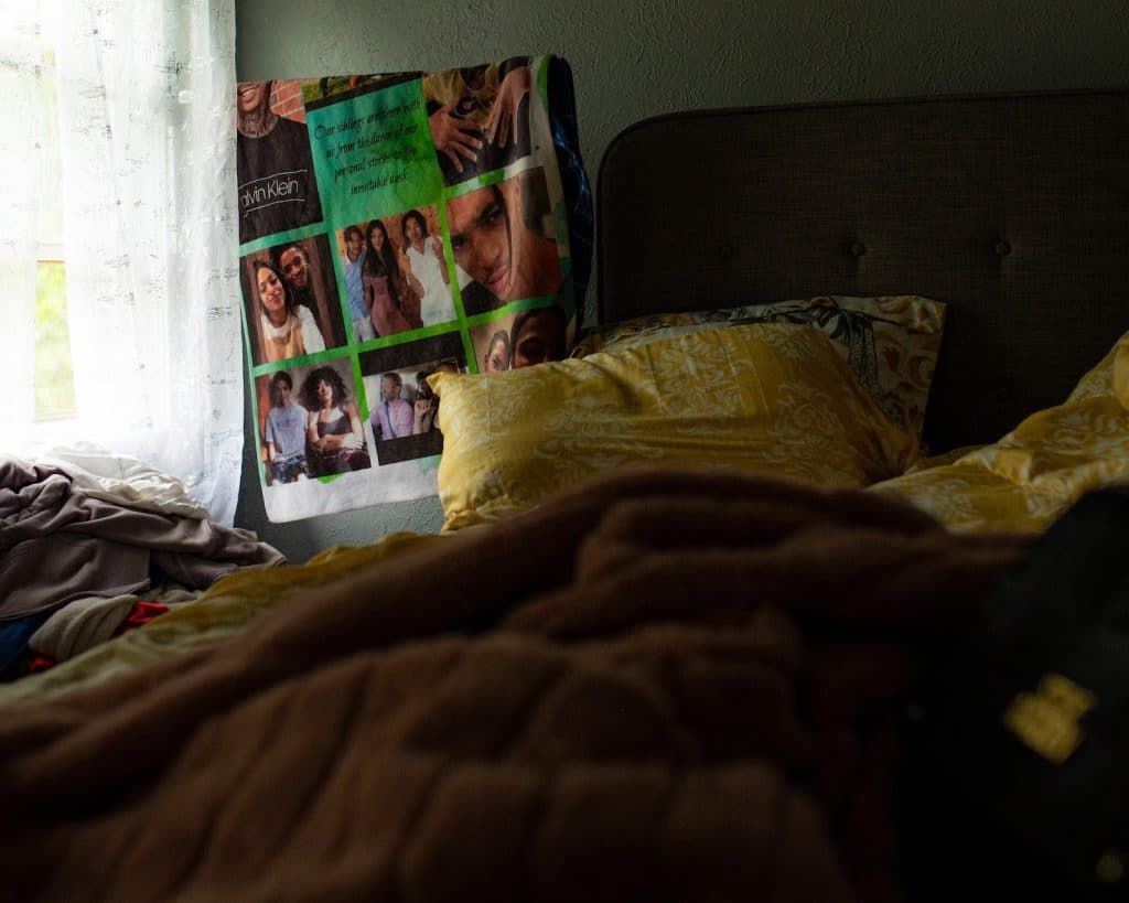 A photo of a green blanket with family photos and text hanging up near a bed with yellow pillows. 