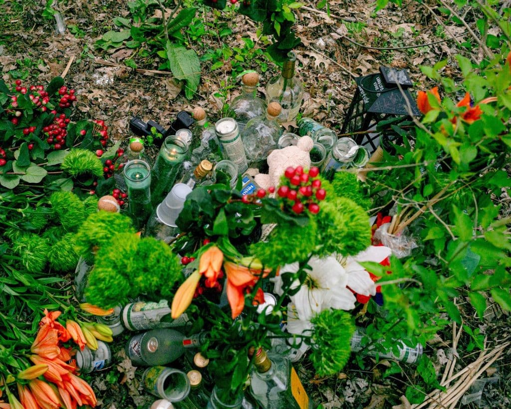 Left: A photo of memorial flowers, candles and drinks on the ground outdoors. 