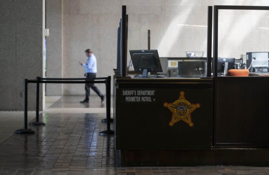 A sectioned off area inside the Cuyahoga County Justice Complex labeled “Sheriff’s Department Perimeter Patrol” has computers and chairs. A man in a long-sleeved button-down shirt and dark-colored pants walks towards the left, behind the sectioned off area.